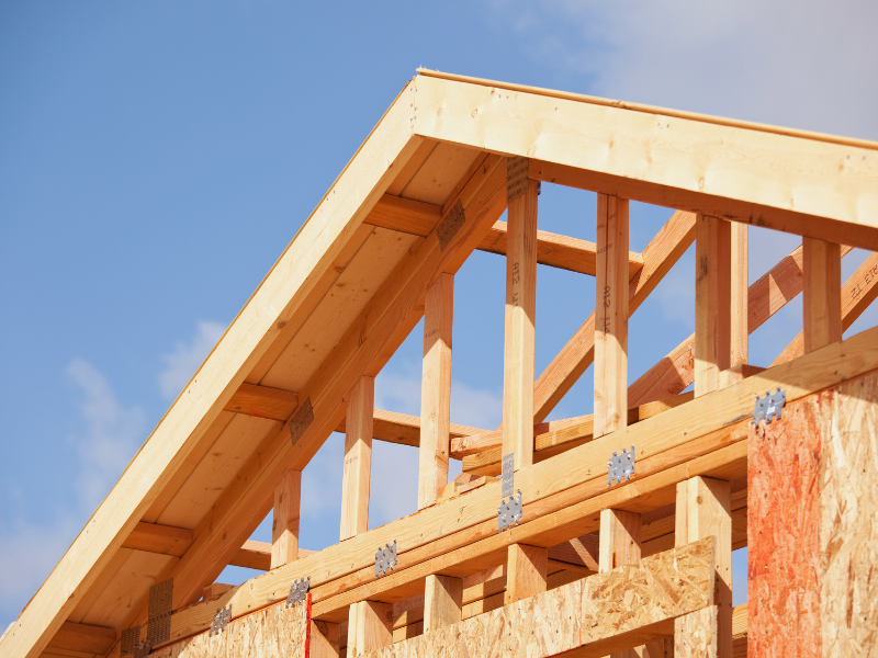A partially constructed wood roof against a blue sky.